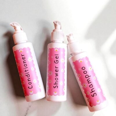 Three bottles with pink daisy-patterned labels on a white background, reading 