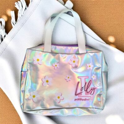 A holographic tote bag with pink and white daisy designs on a soft blanket. The word "Lolly" and the flowers add a playful vibe.