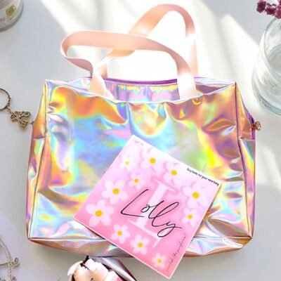 Holographic tote bag with white handles on a white surface, accompanied by a pink sheet with daisy patterns reading