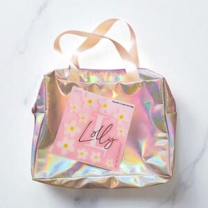 Iridescent tote bag with white handles on a marble surface. A pink sheet with white daisies, the word 
