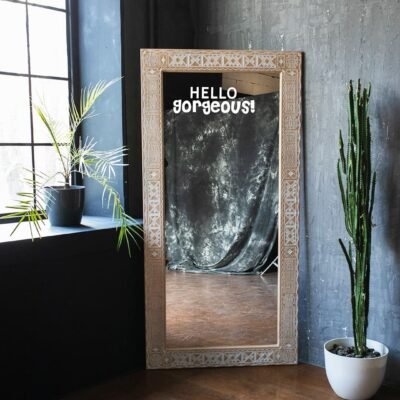 A decor-friendly mirror with a charming message 'HELLO gorgeous!' set against a stylish background and a vibrant plant.