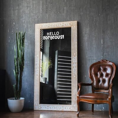 Stylish mirror with a wooden frame reflects a cozy room, featuring a welcoming message, 'Hello Gorgeous!'