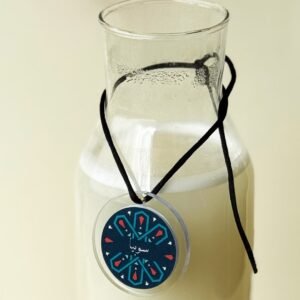 Glass bottle filled with a creamy beverage, adorned with a decorative circular tag featuring geometric patterns and Arabic script, evoking a serene and artistic vibe.