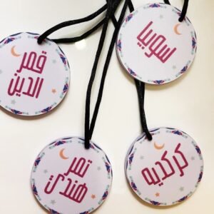 Round tags with black strings, each featuring Arabic text. The tags have colorful borders with crescent moon and star motifs, conveying a festive tone.