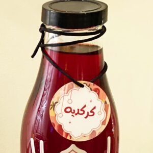 A glass bottle filled with dark red liquid features a black screw cap and a decorative label tied with string, displaying Arabic script in white.
