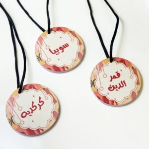 Three round name tags with Arabic text hang on black cords. Each tag has a colorful, decorative border with a festive, cheerful tone.