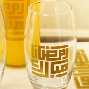 A clear glass with Arabic calligraphy in gold, displaying intricate, geometric patterns. A warm, inviting tone with a gradient yellow background.