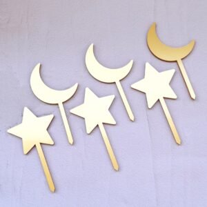 Gold star and crescent moon cupcake toppers against a light pink background. The arrangement is alternating, creating a playful, whimsical feel.