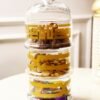 A three-tiered glass jar with decorative gold patterns. The top contains dates, the middle features nuts, and the bottom holds candy. The atmosphere feels elegant and luxurious.