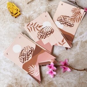 Elegant cards with Arabic calligraphy and abstract designs in beige and pink tones, adorned with floral accents, twine, and a yellow lantern.
