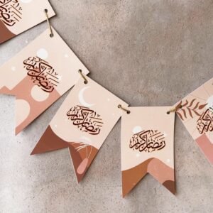 Festive banners with Arabic calligraphy on peach and brown backgrounds, featuring crescent moons and abstract designs, over a gray surface.