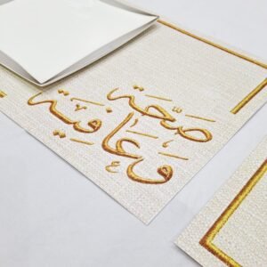 A white, square plate sits on a beige placemat with elegant Arabic calligraphy in gold. The setting is clean and sophisticated, conveying a sense of warmth and hospitality.