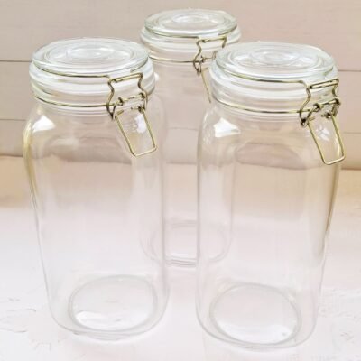 Three clear glass jars with metal clasps are arranged on a light wooden surface. They convey a clean, minimalist aesthetic, suitable for storage.