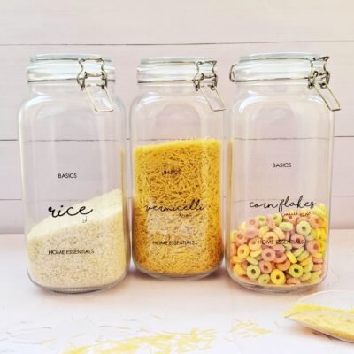 Three clear jars with metal clasps labeled “rice,” “vermicelli,” and “cornflakes.” Each jar is filled with its respective content, styled on a light wood surface.