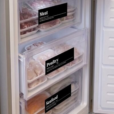 Open freezer with organized transparent drawers labeled for meat, poultry, and seafood. Packs neatly arranged; veggies visible in the top drawer.