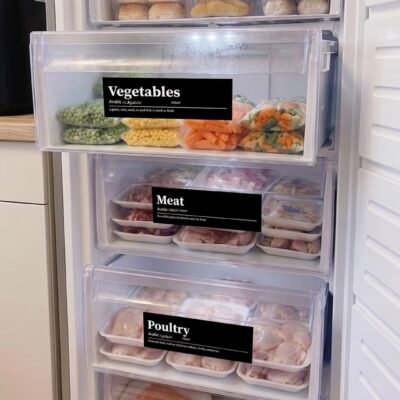 Open freezer with organized labeled drawers. Top to bottom: baked goods, vegetables, meat, poultry, and seafood, in transparent trays. Clean and orderly tone.