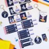 Flat lay of colorful Omar M. Ali stickers, labels, and keychains with playful astronaut designs, plus pens, scissors, and folders.