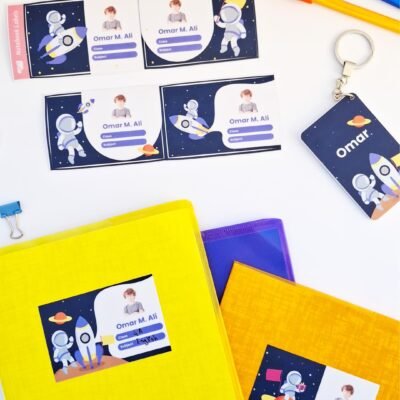 Colorful astronaut-themed ID cards and badges labeled “Omar M. Ali,” displayed with bright folders, keychain, and markers on a white background.
