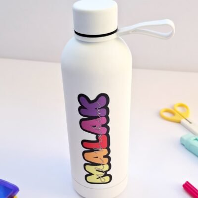 White reusable water bottle with a loop cap and colorful playful lettering, standing on a desk beside scissors and craft supplies in soft light.