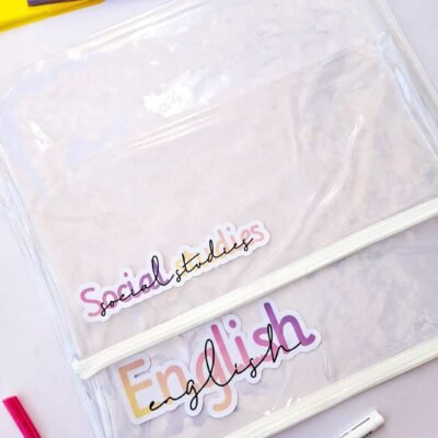 Transparent files labeled “Social Studies” and “English” lie on a desk with colorful notebooks and pens, creating a cheerful study scene.