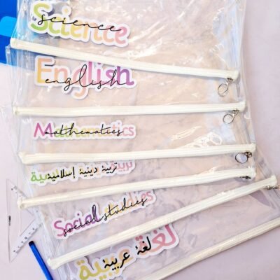 Stack of transparent zippered school files labeled Science, English, Mathematics, Islamic Studies, Social Studies, and Arabic, with pens.