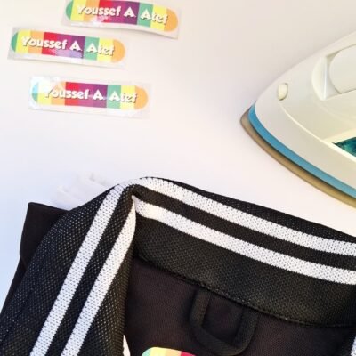Black-and-white striped jacket with a colorful label, matching stickers above, and a white-and-teal iron nearby. Playful tone.