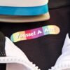 Colorful “Youssef A. Atef” name tag rests on black fabric between white fabric and a blue-and-white iron, creating a playful, personal tone.