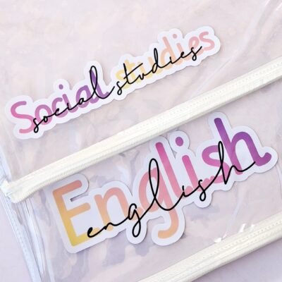 Transparent files with playful pink-and-yellow “Social Studies” and “English” stickers, white zippers, and a pen on a soft background.