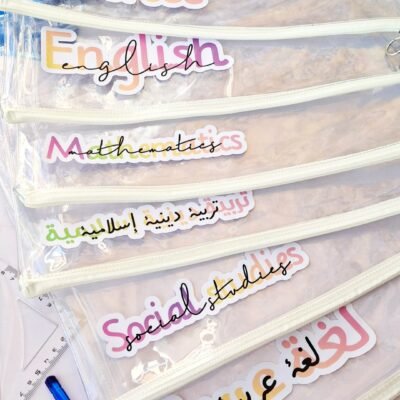 Stacked clear school files labeled Science, English, Mathematics, Islamic Studies, Social Studies, and Arabic in colorful lettering; cheerful.